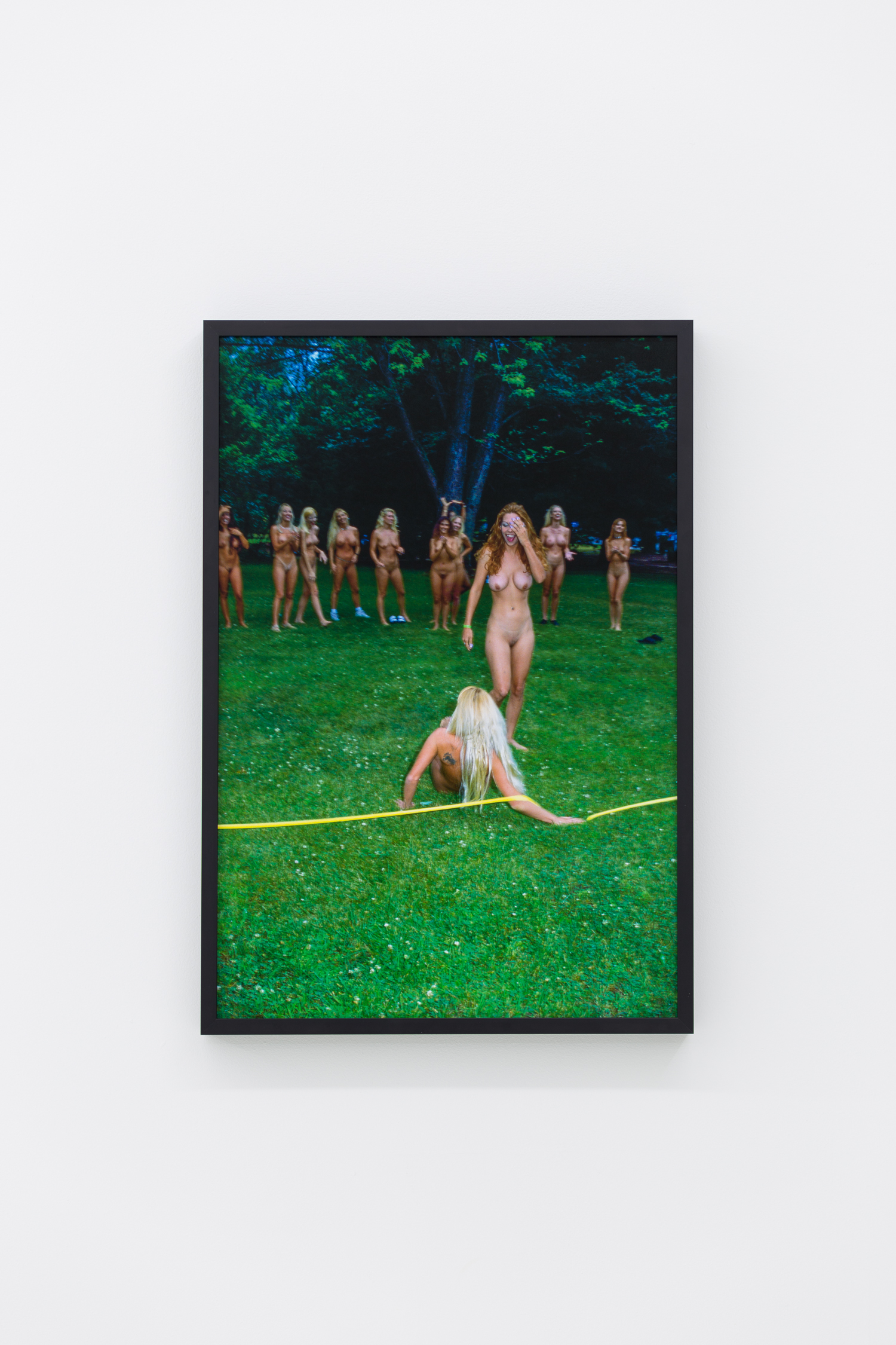 Photo of many naked women in a park, one lies on the ground, her arm twined around a yellow rope